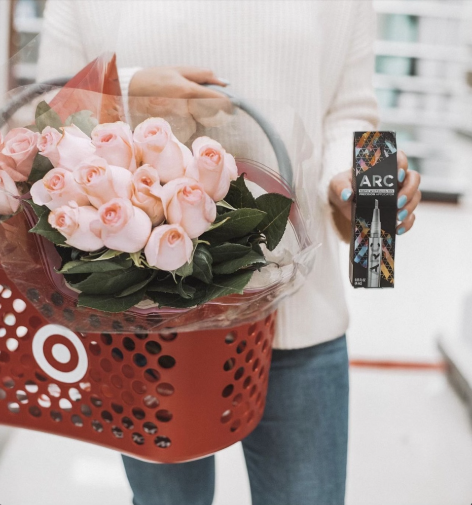 A woman holds a shopping basket full of flowers along with a beauty product