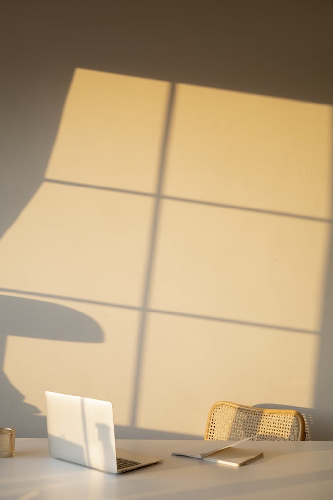 A serene minimalist workspace with natural light casting shadows on a wall, featuring a laptop.